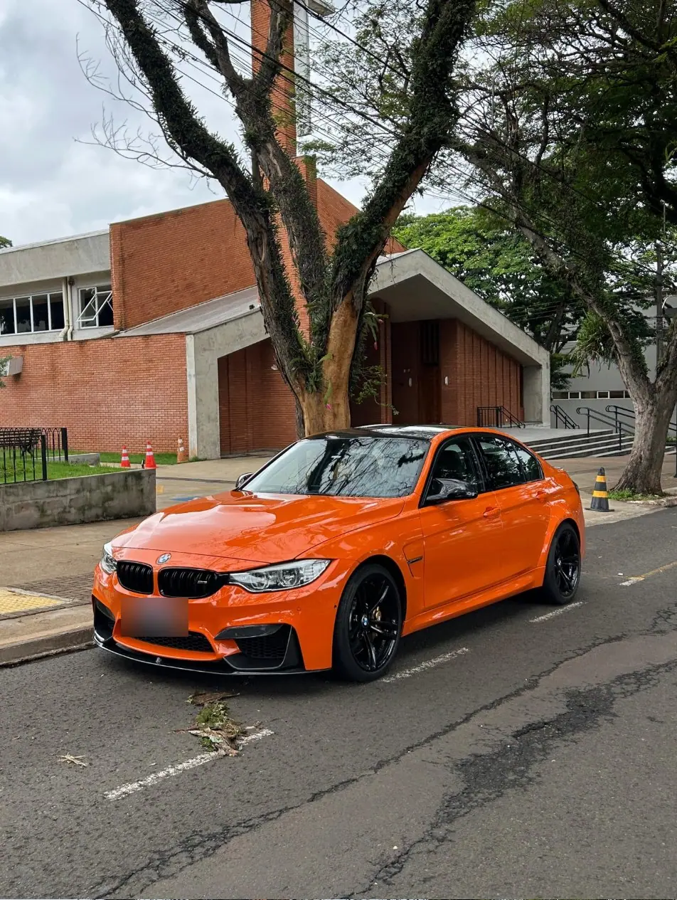 BMW M3 laranja estacionado em frente a um prédio de tijolos