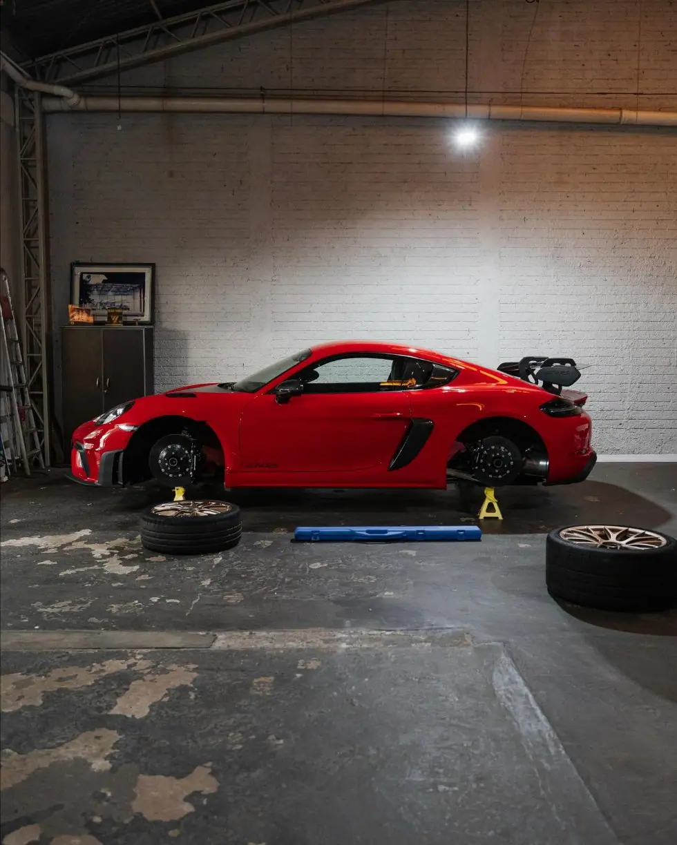 Porsche 718 GT4 RS vermelho de perfil, sobre cavaletes, na oficina APEX